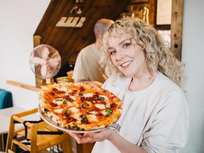 Woman holding up a wood-fired pizza on her plate